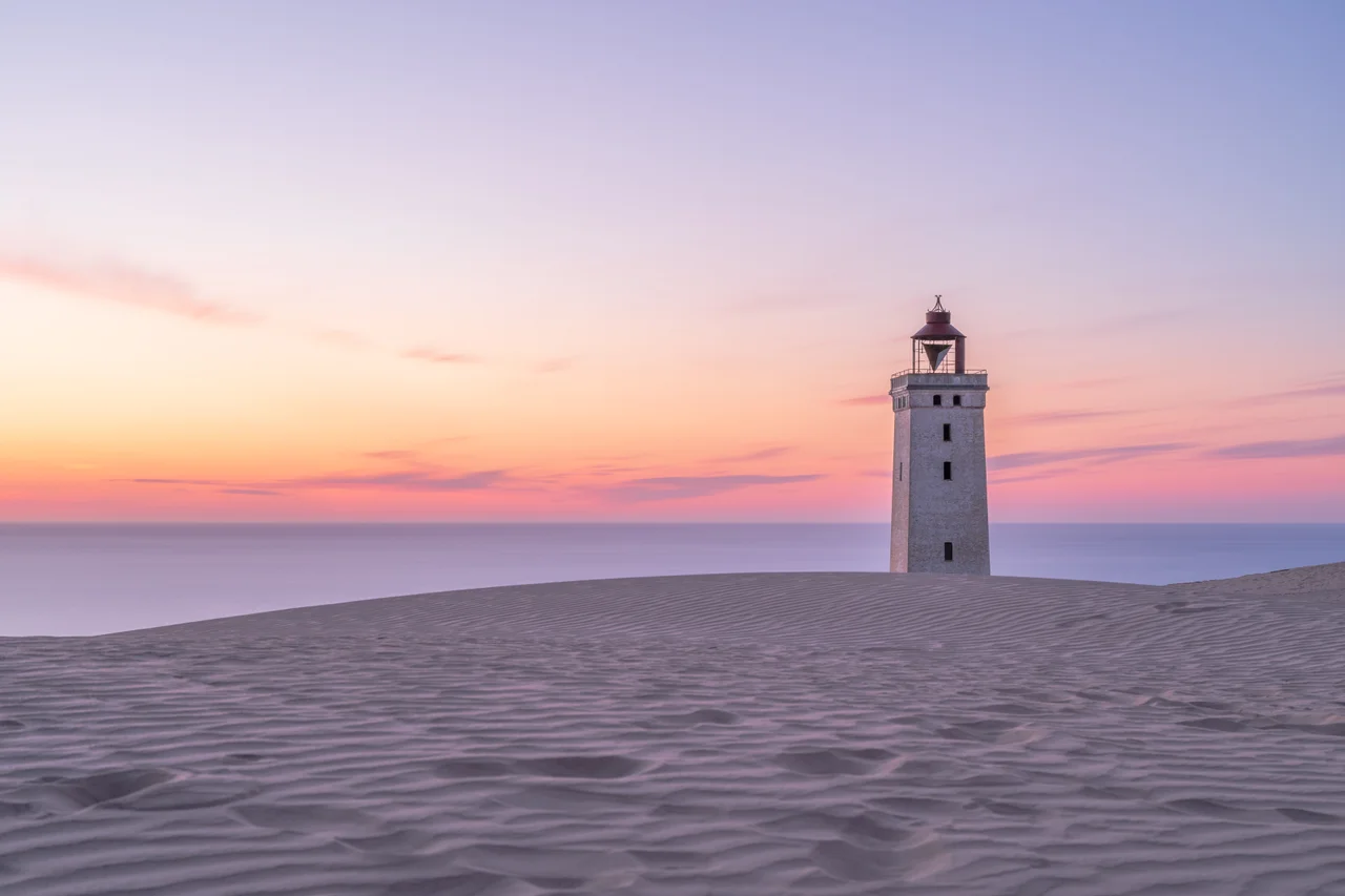 Rubjerg Knude Fyr is a lighthouse between Lønstrup and Løkken (municipality Hjørring) in Denmark which was built in 1900. From the 1910s, the wind blew large amounts of sand from the cliffs and the actual dune formed between the lighthouse and the sea. The dune moved towards northeast and now has completely passed the lighthouse. Of the outbuildings only loose bricks remains. The lighthouse was built 200 m from the coast, but the sea has since eaten into the 60 m high cliff so much that the lighthouse is now in grave danger of falling into the sea . It's now planned to move it 60-80 meters inland, which should protect it another 40-60 years.